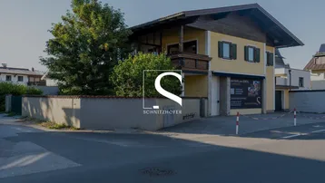 Gebäude mit gelber Fassade, Holzbalkonen und ummauertem Vorgarten an einer Straße.
