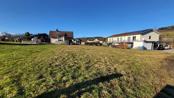 Weitläufiges Grundstück mit grüner Wiese und umliegenden Wohnhäusern unter blauem Himmel.
