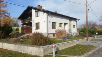 Einfamilienhaus mit Satteldach, kleinem Vorgarten und Balkon im Obergeschoss unter blauem Himmel.