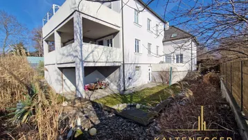 Rückseite des Hauses mit mehreren Balkonen und einem naturbelassenen Gartenbereich mit trockenen Pflanzen.