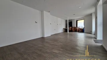 Weitläufiger Geschäftsraum mit Laminatboden und einem Bereich im Hintergrund, der für Lagerung genutzt werden könnte.