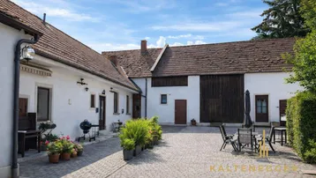 Gepflasterter Innenhof mit Sitzgelegenheiten und Grillbereich zwischen den Gebäuden.