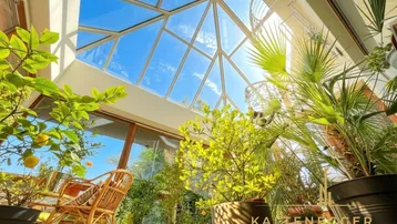 Heller Wintergarten mit Glasdach und vielen Pflanzen, ideal für entspannte Stunden und viel Tageslicht.