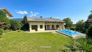 Rückseite des Hauses mit großem Garten, einem Pool mit Überdachung und Solarpaneelen auf dem Dach.