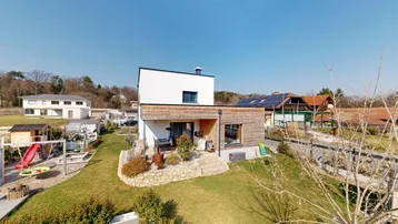 Gesamtansicht des modernen Hauses mit großem Garten, Spielplatz und Photovoltaikanlage auf dem Dach.