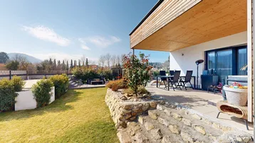 Große Terrasse mit Gartenmöbeln und Blick ins Grüne, umgeben von einem gepflegten Rasen und Steinmauern.