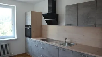 Moderne Einbauküche mit grauen Fronten, Holzdetails, integriertem Backofen und Dunstabzugshaube.