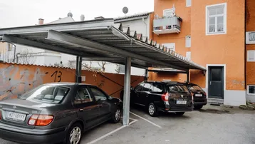 Außenbereich mit überdachten Parkplätzen und orangefarbener Gebäudefassade.