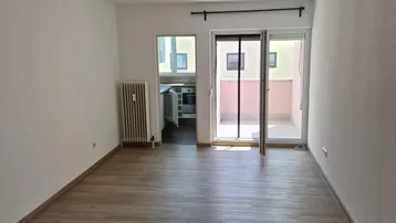 Helles Wohnzimmer mit Laminatboden, Heizkörper und Zugang zum Balkon, bereit zur Einrichtung.