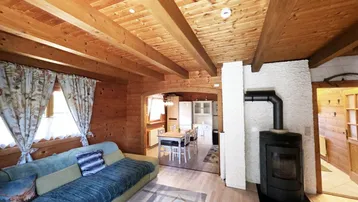 Gemütliches Wohnzimmer mit Holzbalkendecke, Kaminofen und Blick in die offene Küche.