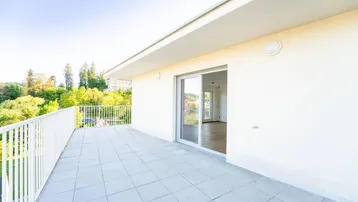 Helle, geflieste Terrasse mit weißem Geländer und Zugang zu einem lichtdurchfluteten Innenraum.