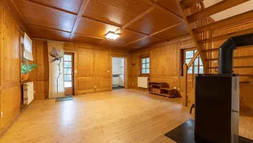 Gemütliches Wohnzimmer mit Holztäfelung, Holztreppe und einem traditionellen Kaminofen.