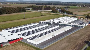 Luftaufnahme einer modernen Garagenanlage mit Photovoltaikanlagen auf den Dächern, umgeben von Feldern.