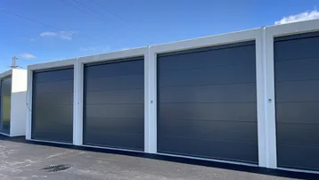Reihe moderner Garagentore in Anthrazit mit weißem Rahmen unter blauem Himmel.