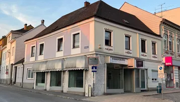 Historisches Gebäude an einer Straßenecke mit Geschäften im Erdgeschoss und Wohnungen darüber.
