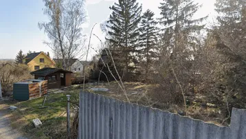 Blick auf ein Grundstück mit Garten, einem kleinen Schuppen und einem gelben Haus im Hintergrund.