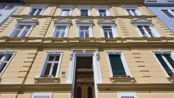 Historische Fassade eines Mehrfamilienhauses in hellem Gelb mit vielen Fenstern und Verzierungen.