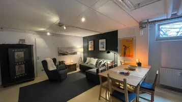 Helles Wohn- und Esszimmer mit dunklem Teppich, Holztisch und gemütlicher Sitzecke.