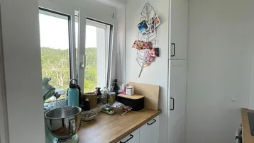 Helle Küche mit Holz-Arbeitsplatte, weißen Schränken und Fenster mit Ausblick.