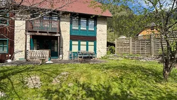 Charmantes Haus mit rotem Dach, Balkon und Terrasse, umgeben von einem grünen Garten.