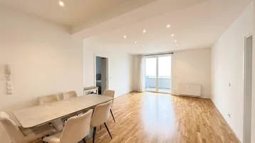 Heller Wohn- und Essbereich mit Parkettboden, moderner Beleuchtung und Zugang zum Balkon.