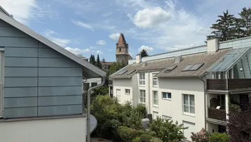 Blick über die Dächer der umliegenden Gebäude mit einem historischen Turm im Hintergrund.