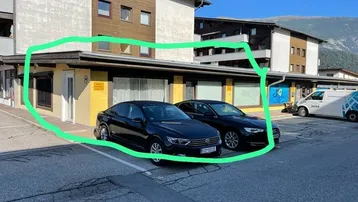 Außenansicht eines Gewerbegebäudes mit Parkplätzen und Bergkulisse im Hintergrund.