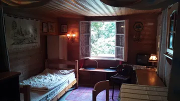 Rustikales Schlafzimmer mit Holzwänden, Einzelbett und Fenster mit Blick ins Grüne.
