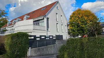 Außenansicht eines Wohngebäudes mit rotem Ziegeldach, weißer Fassade und barrierefreiem Zugang über eine Rampe.