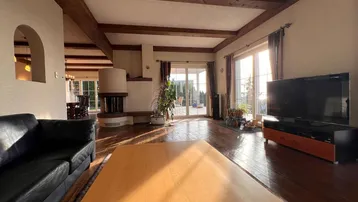 Helles Wohnzimmer mit Holzbalken, Kamin und Zugang zur Terrasse mit viel Tageslicht.