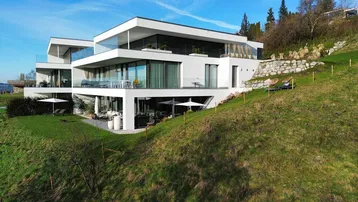 Moderne Architektur einer Villa am Hang mit großen Fensterfronten und Terrassen.