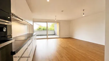 Heller offener Wohnbereich mit integrierter Küche, Holzboden und Zugang zu einem Balkon.