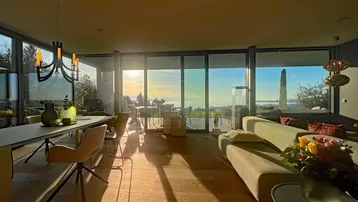 Helles Wohn- und Esszimmer mit Seeblick, großen Fenstern und modernem Interieur bei Sonnenuntergang.