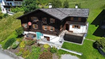 Luftaufnahme des traditionellen Holzhauses mit umliegendem Garten und grünen Hügeln.
