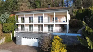 Großzügige Villa mit mehreren Balkonen, Doppelgarage und umgebender Natur mit Pool.