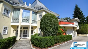Elegante Fassade eines Hauses mit gepflegtem Vorgarten und geschwungenem Eingangsbereich unter blauem Himmel.