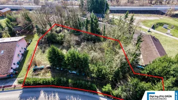 Luftaufnahme eines Grundstücks mit roter Umrandung, umgeben von Bäumen und einer Straße.