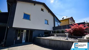 Modernes Einfamilienhaus mit weißer und anthrazitfarbener Fassade und gepflegtem Vorgartenbereich.