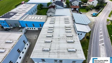 Luftaufnahme eines Industriegebiets mit mehreren Hallen und umliegender Landschaft unter bewölktem Himmel.