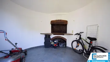 Abstellraum mit gemauertem Grill oder Kamin, Fliesenboden und Stauraum für Gartengeräte.