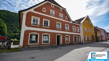 Traditionelles Gebäude mit roter Fassade und weißen Fensterrahmen in ländlicher Umgebung.