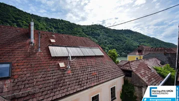 Dachlandschaft mit Ziegeln und Solarpaneelen, bietet einen weiten Blick auf einen Fluss und grüne Hügel.