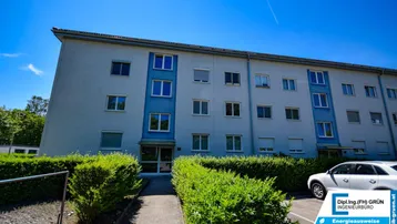 Mehrstöckiges Wohngebäude mit hellblauer Fassade und gepflegter Hecke im Vorgartenbereich.