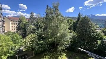 Weitläufiger Blick ins Grüne mit altem Baumbestand und majestätischen Bergen im Hintergrund.