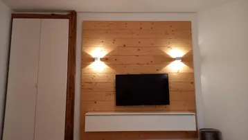 Wohnzimmer mit moderner Holzvertäfelung, integriertem TV und weißem Schrank.