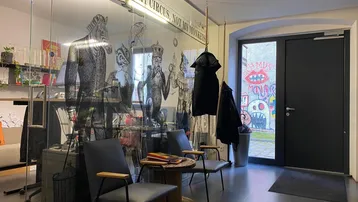 Moderner Büroeingangsbereich mit Glaswand, bequemen Sitzgelegenheiten und Blick auf eine kreativ bemalte Außenwand.
