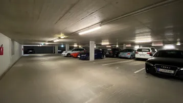Geräumige Tiefgarage mit Betonboden und -decke, beleuchtet von Leuchtstoffröhren, bietet Platz für mehrere Fahrzeuge.
