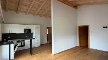 Heller offener Wohnbereich mit Holzbalkendecke, Parkettboden und integrierter Küche.