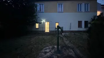 Hausfassade bei Dämmerung mit beleuchteten Fenstern und Gartenbereich.