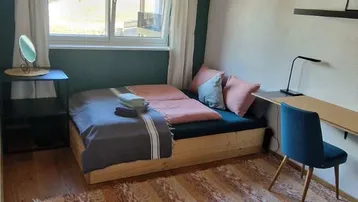 Gemütliches Schlafzimmer mit Holzbalkendecke, Teppichboden und einem Schreibtischbereich am Fenster.
